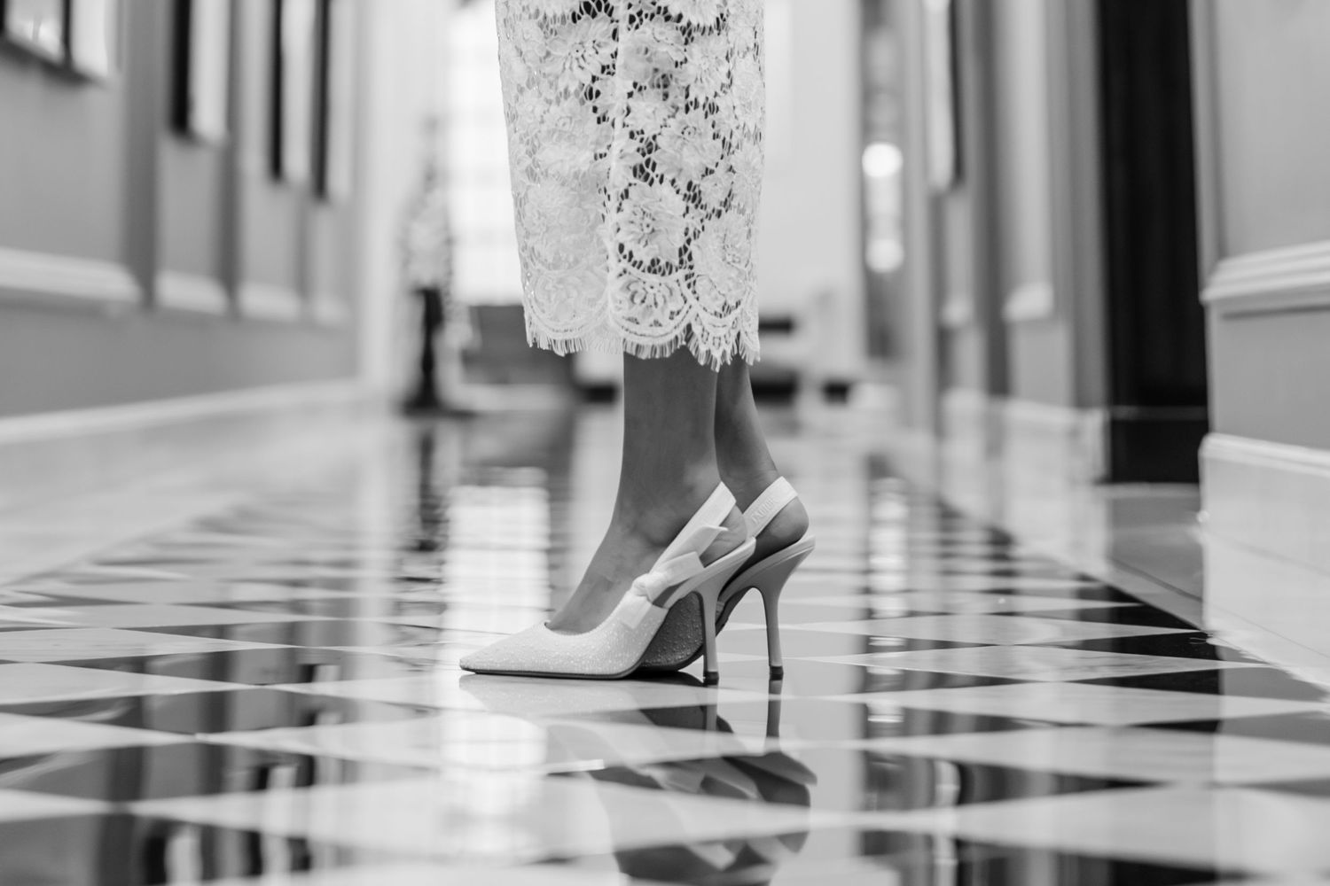 Black and white photo of feet walking on checkered tile floor.