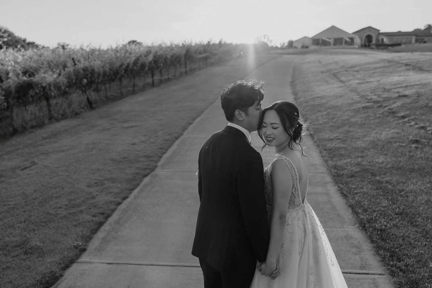 A couple takes romantic wedding photos at sunset on a path through a countryside meadow.