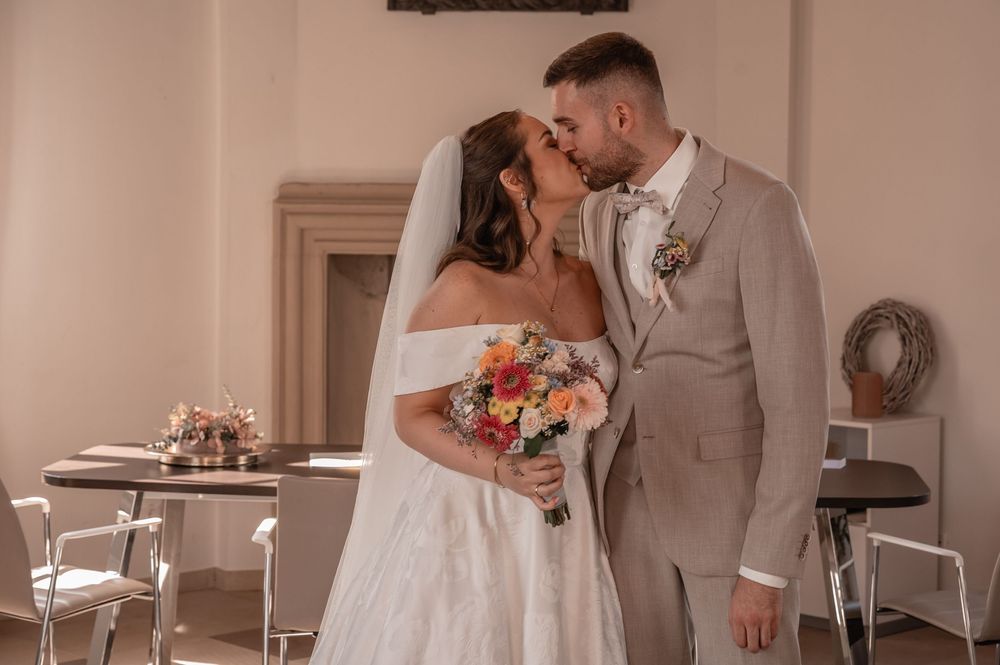 Two figures share an intimate moment under soft indoor lighting at what appears to be a wedding celebration.
