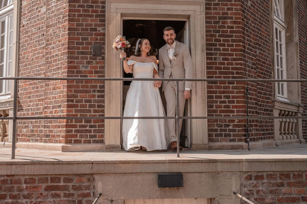 Two people stand elegantly in a brick arched entryway during a summer wedding celebration.
