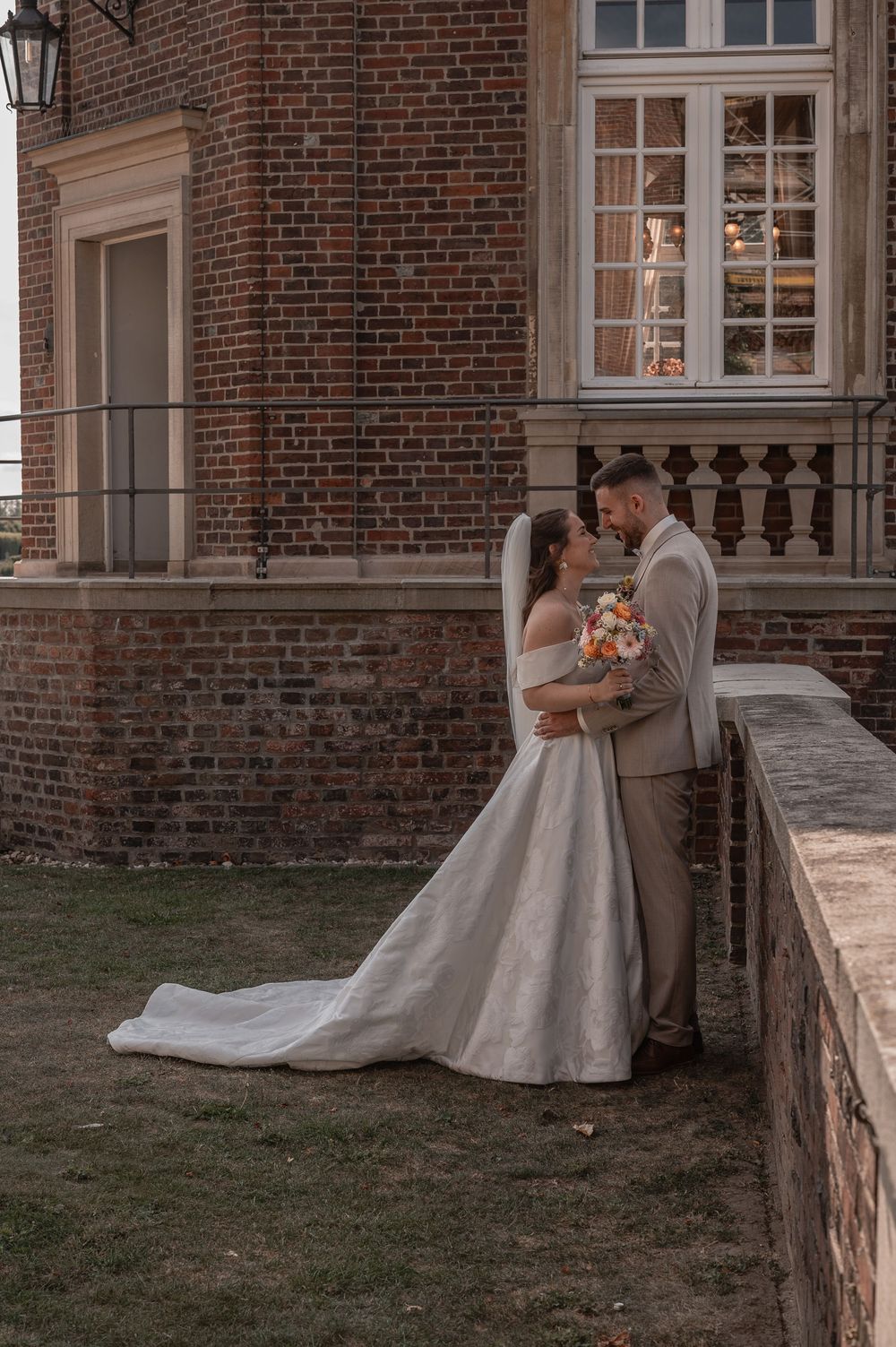 A romantic wedding portrait of a couple embracing in front of a historic brick mansion with a flowing white dress.