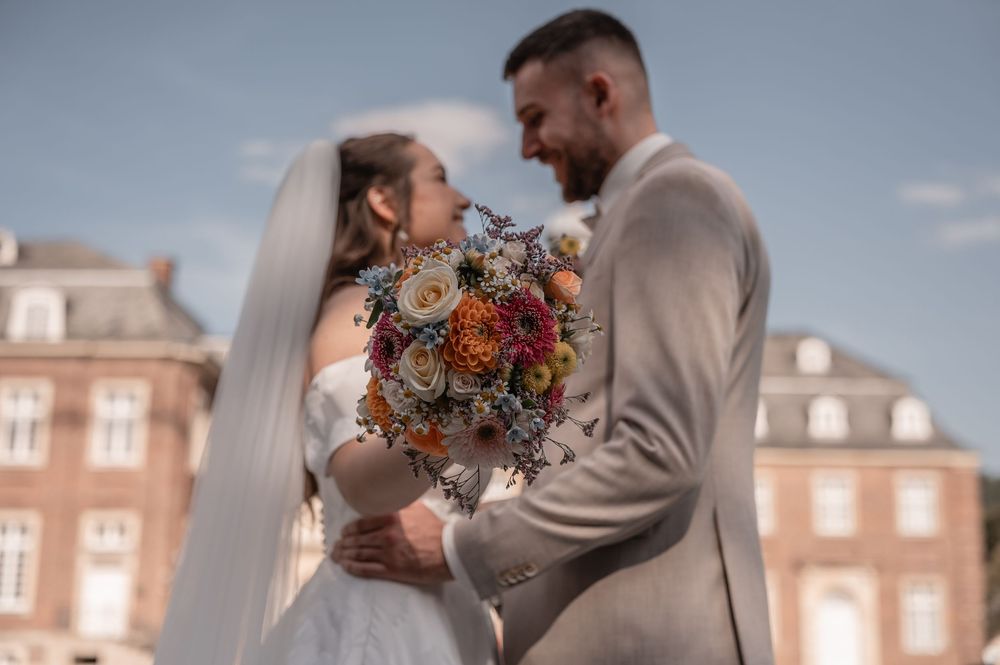 A couple in wedding attire sharing an intimate moment outdoors, with the bride holding a vibrant autumn bouquet.