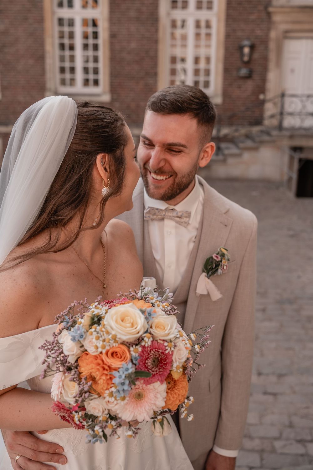 An intimate wedding moment captured with a beautiful floral bouquet against a brick building backdrop.