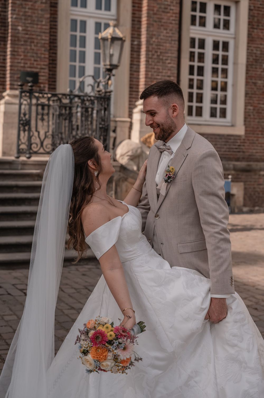 A joyful wedding couple shares a moment on stone steps with the bride holding a vibrant floral bouquet.