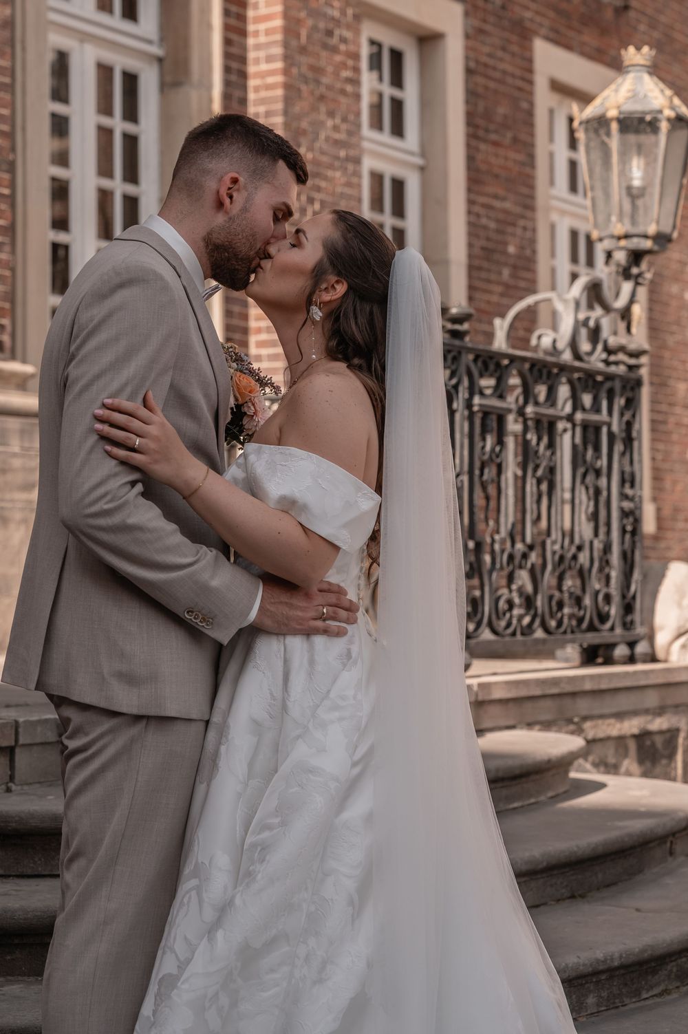 A romantic wedding moment captured at a historic brick building with elegant ironwork and a classic lantern.