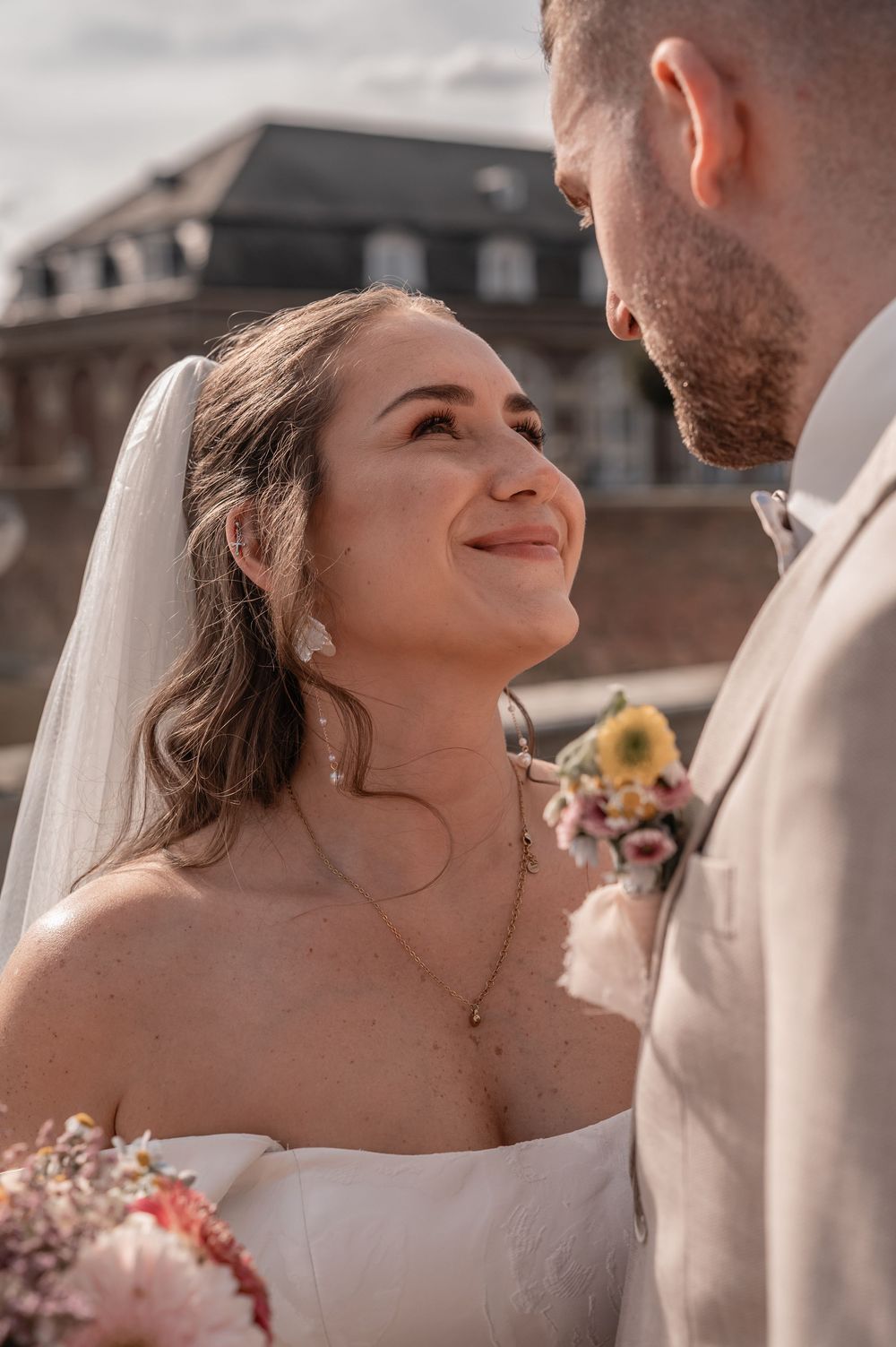 A joyful wedding moment shows a couple gazing at each other outdoors with elegant brick architecture in the background.