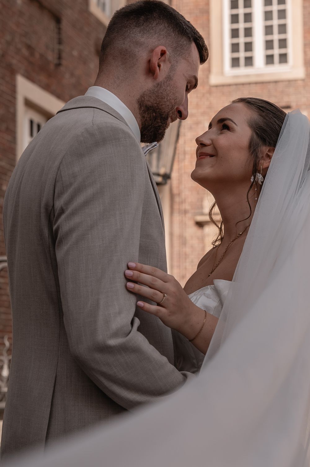 Intimate wedding moment captured of couple in sweet embrace outside historic brick building, bride in white veil.