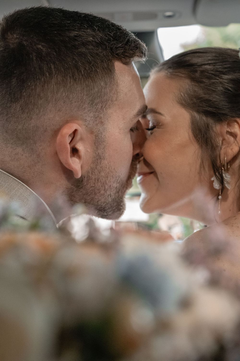 An intimate wedding photo captures a tender moment between newlyweds with soft flowers in the foreground.
