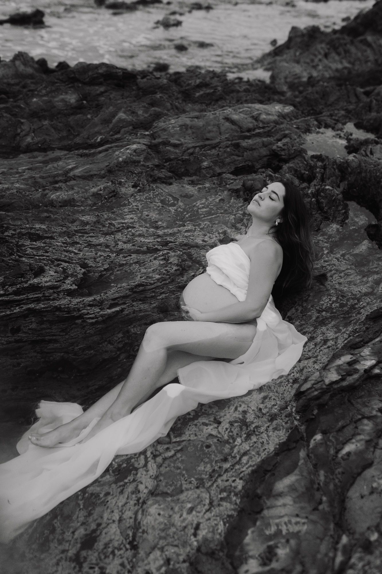 Black and white artistic photo series of someone reclining on coastal rocks.
