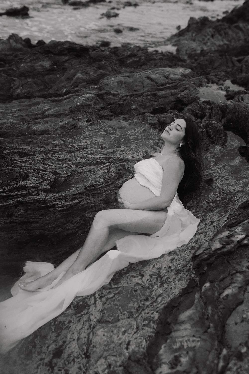 Black and white artistic photo series of someone reclining on coastal rocks.