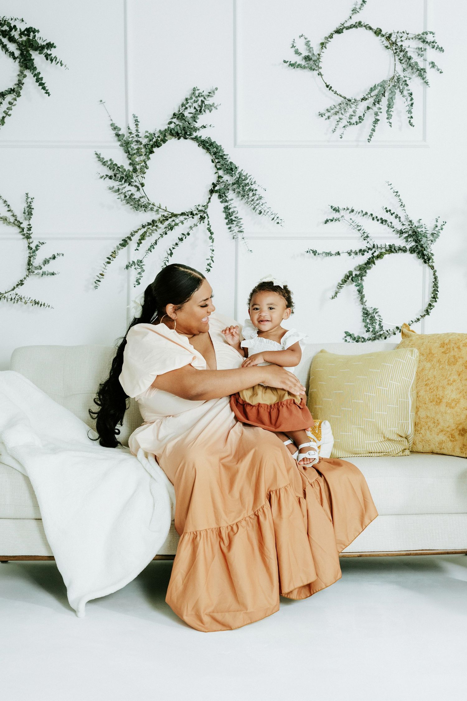 Two people share a joyful moment on a white couch with decorative greenery on the wall.