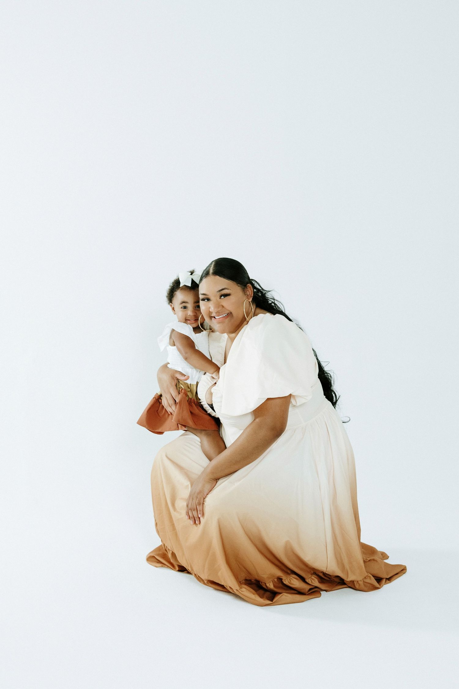A tender moment captured against a white backdrop in coordinated cream and rust outfits.