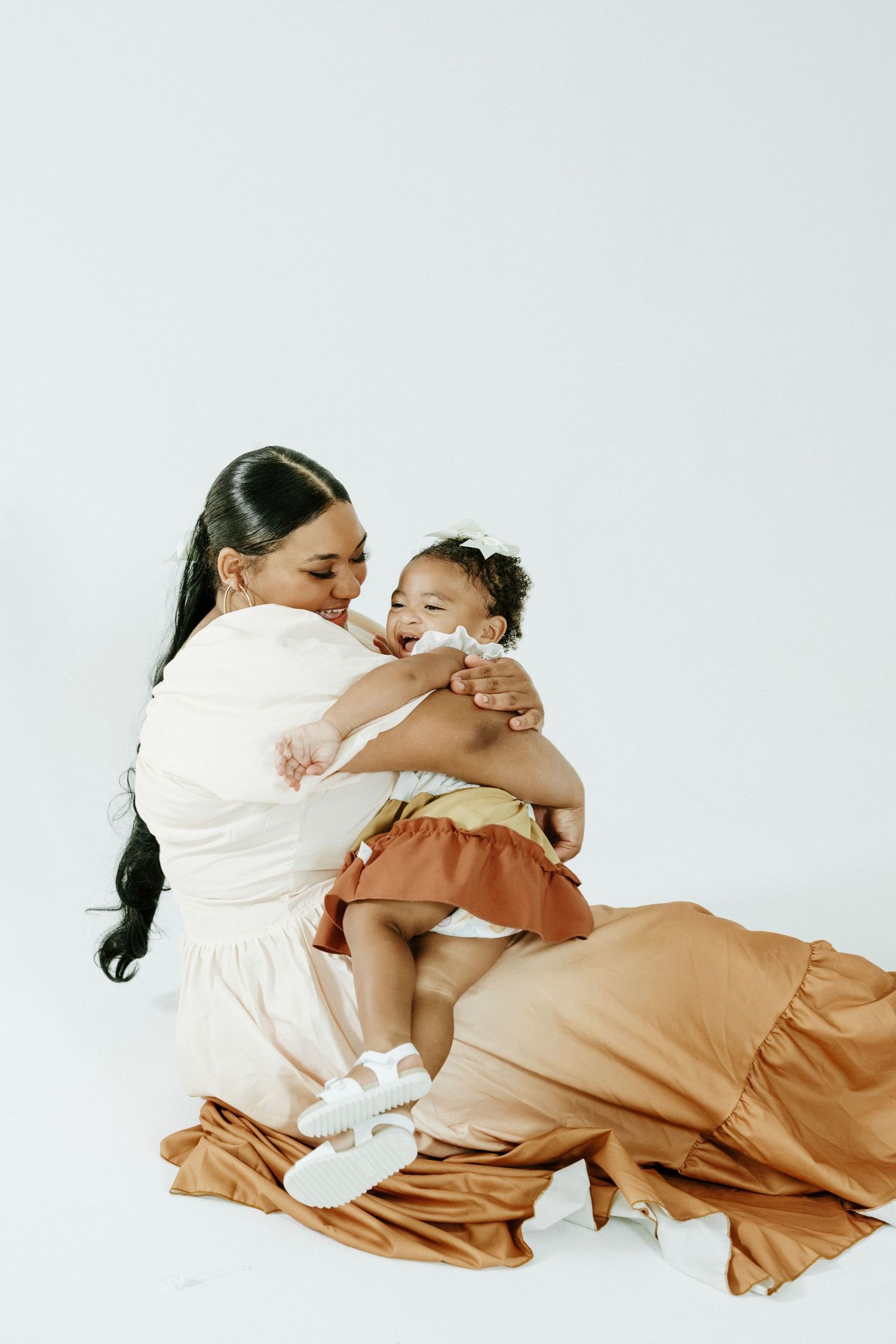 A joyful studio photography session with matching white and tan dresses in a minimalist setting.