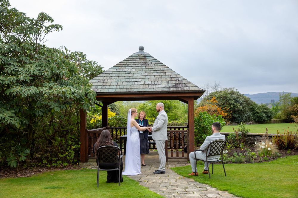 Intimate outdoor wedding ceremony under a wooden gazebo with scenic countryside views in the background.