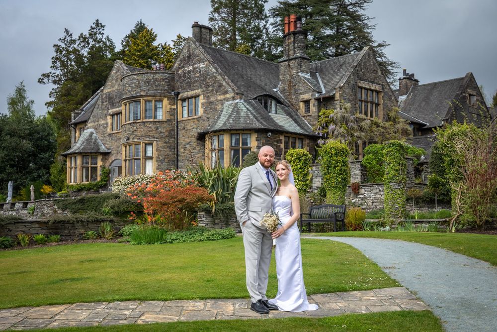 Bride and groom pose together on a garden path in front of a stunning stone country house estate.