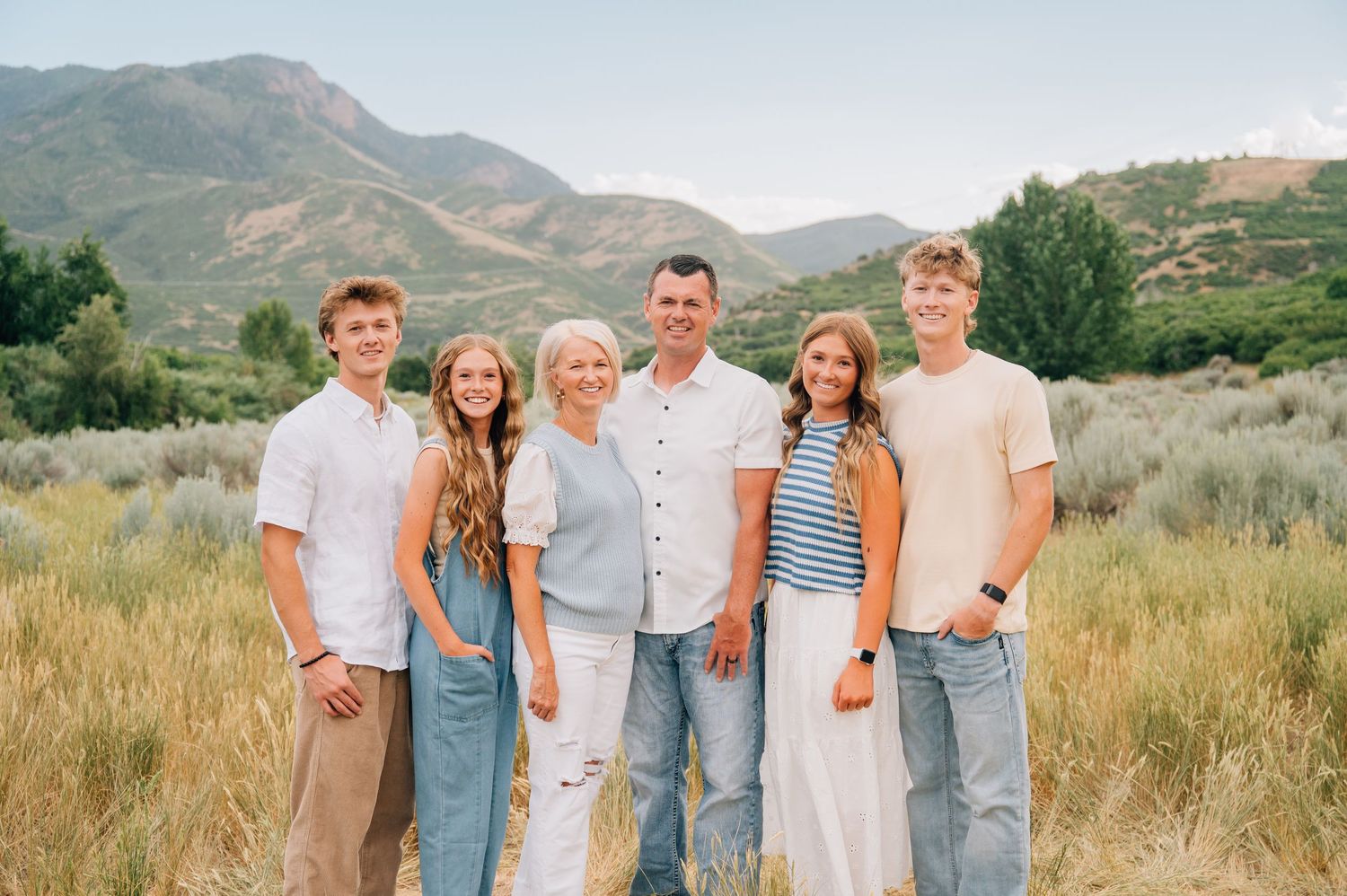 A group standing together in casual attire against a backdrop of mountains and desert brush in warm evening light.