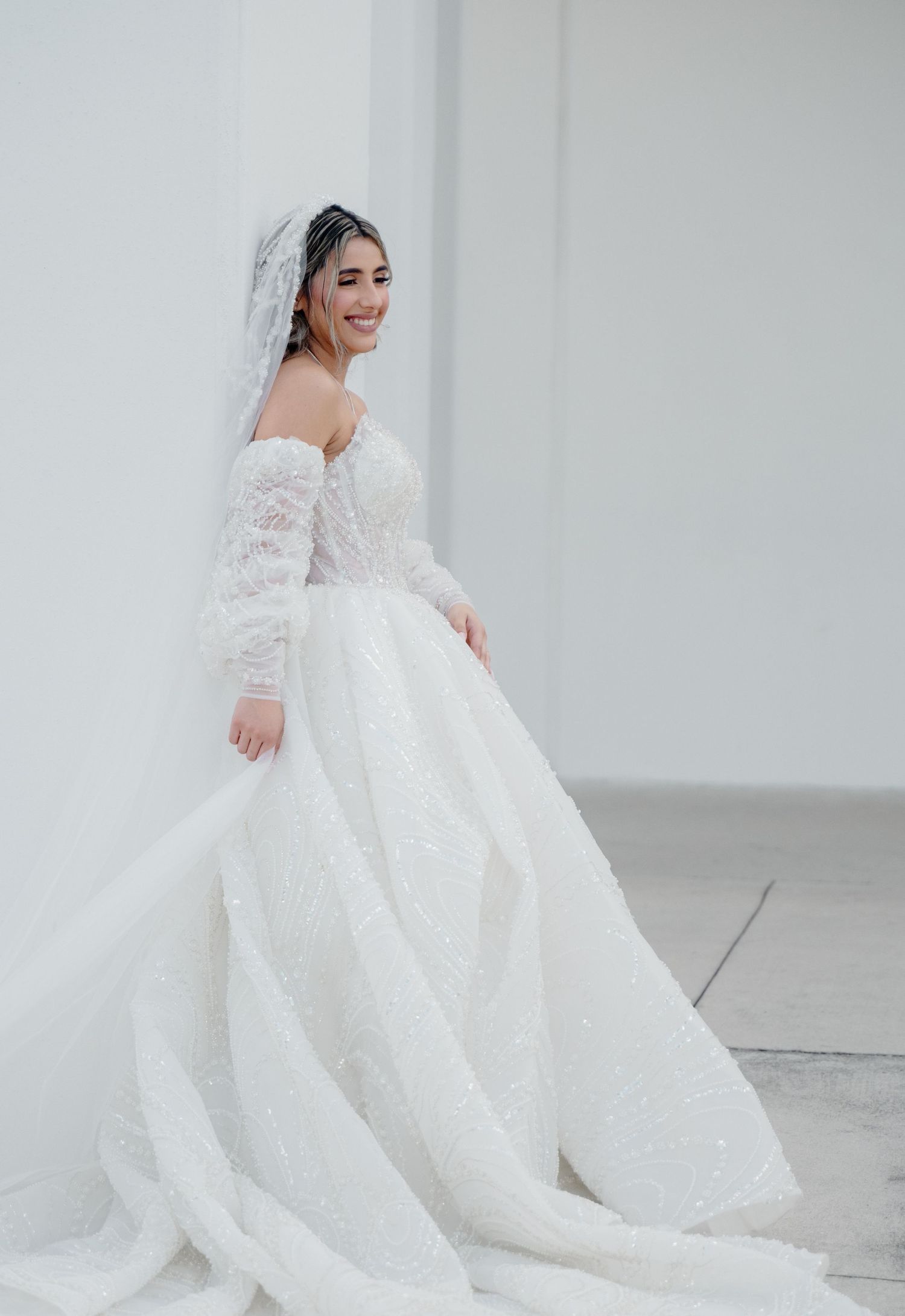 A stunning off-shoulder lace wedding gown with flowing train photographed against a white backdrop.