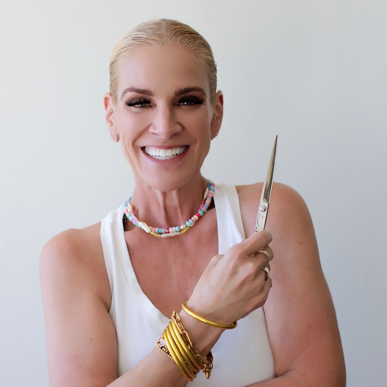 Headshot of a smiling blonde woman hairdresser holding scissors
