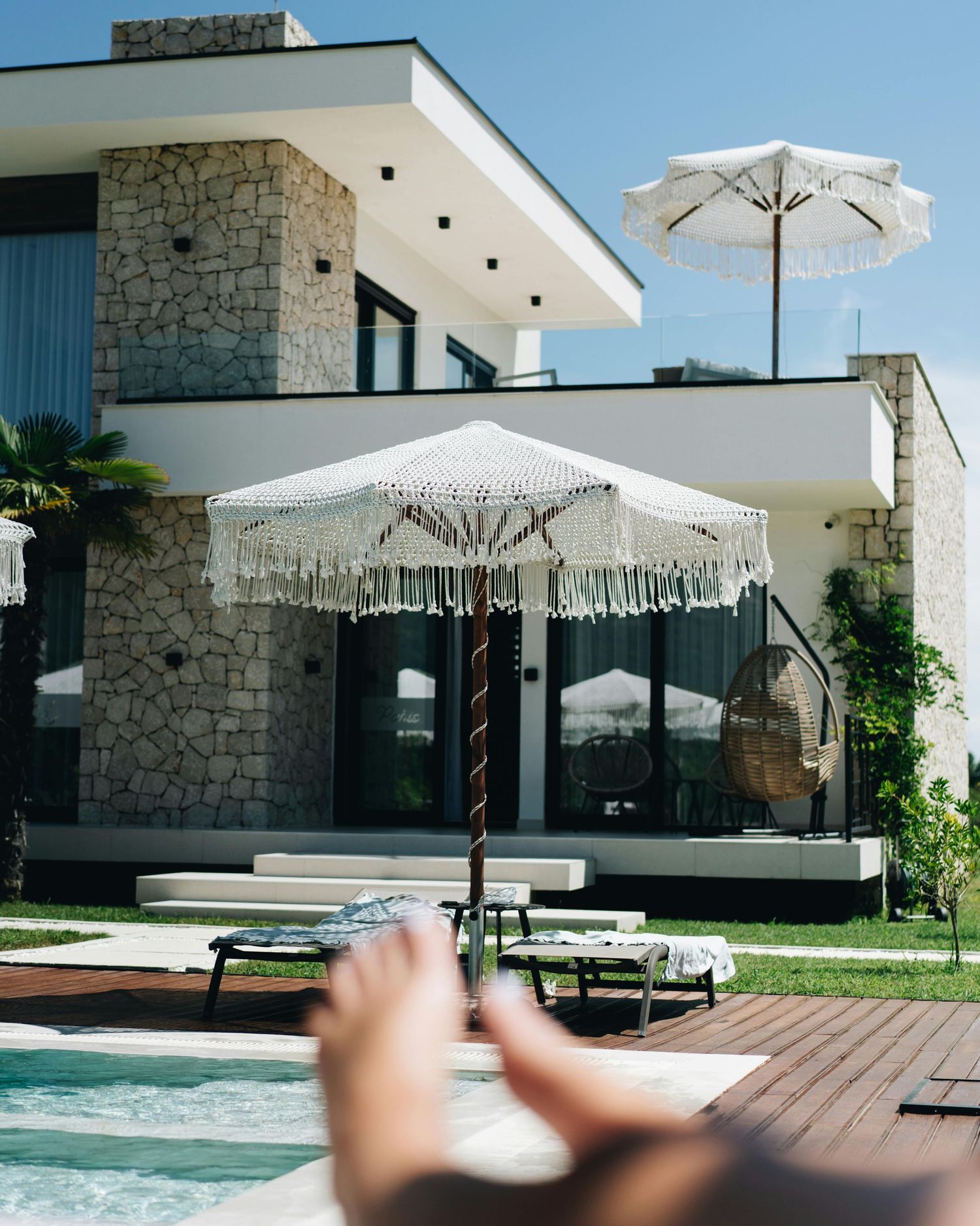 Modern luxury villa with pool deck and white umbrellas on sunny day.