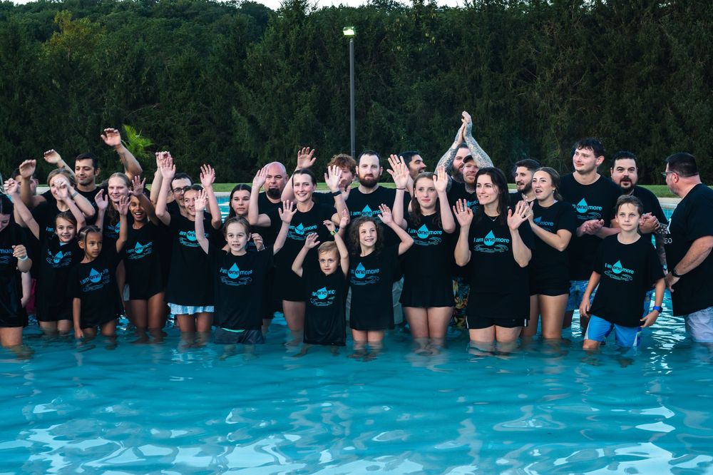 A group engaging in a large pool based mass baptism ceremony at a summer youth retreat.
