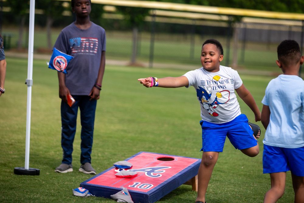 Young boy tossing a bean bag at a cornhole board during an outdoor game on a green field.