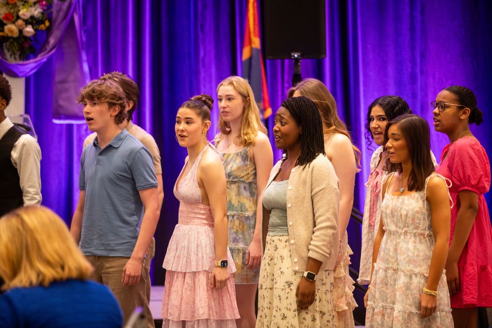 Diverse group of young students performing on stage at a school event, dressed in formal attire under purple lights.