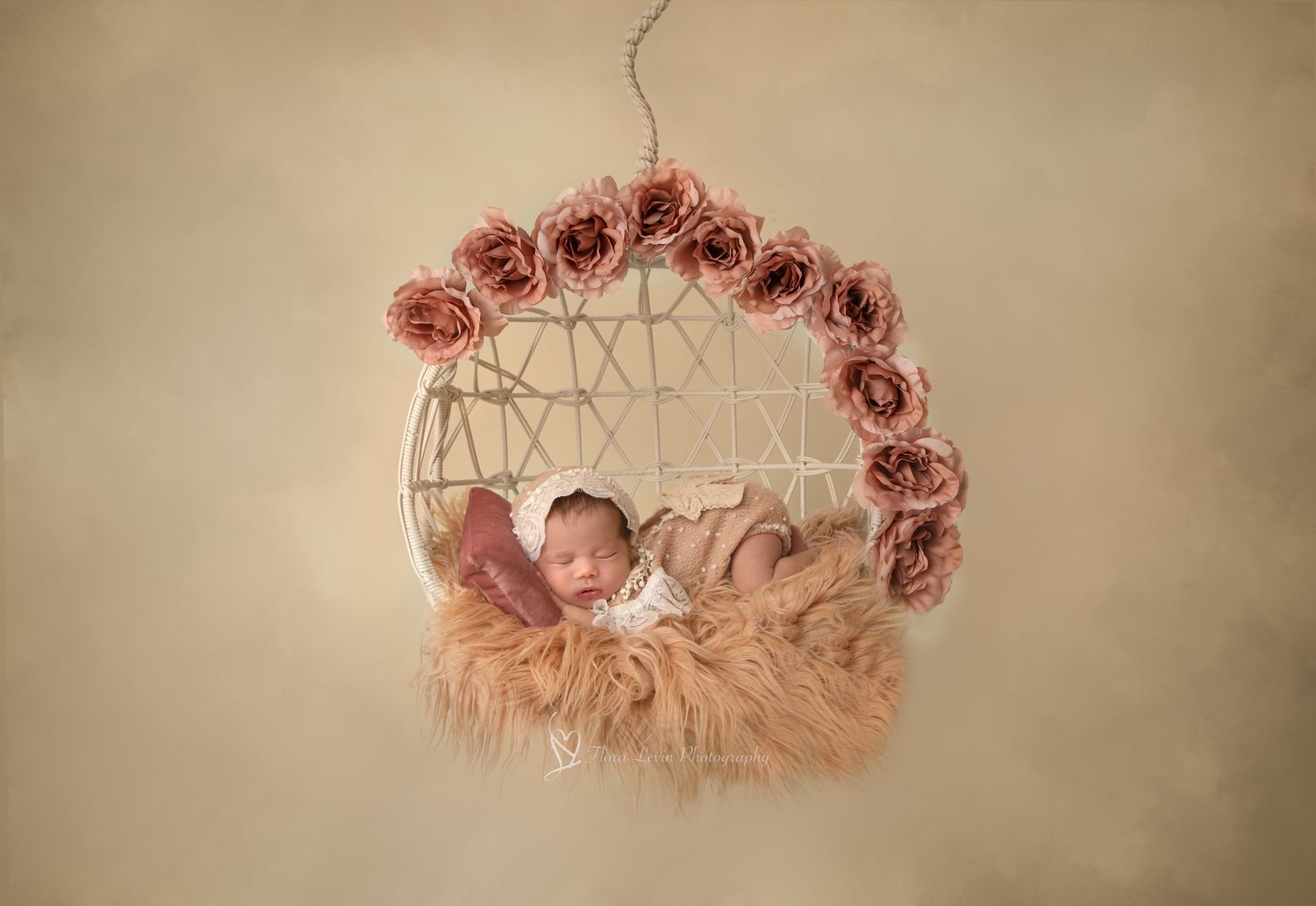 Dust rose toned photo series of a baby girl sleeping in a rustic macrame cradle with pink floral accents.