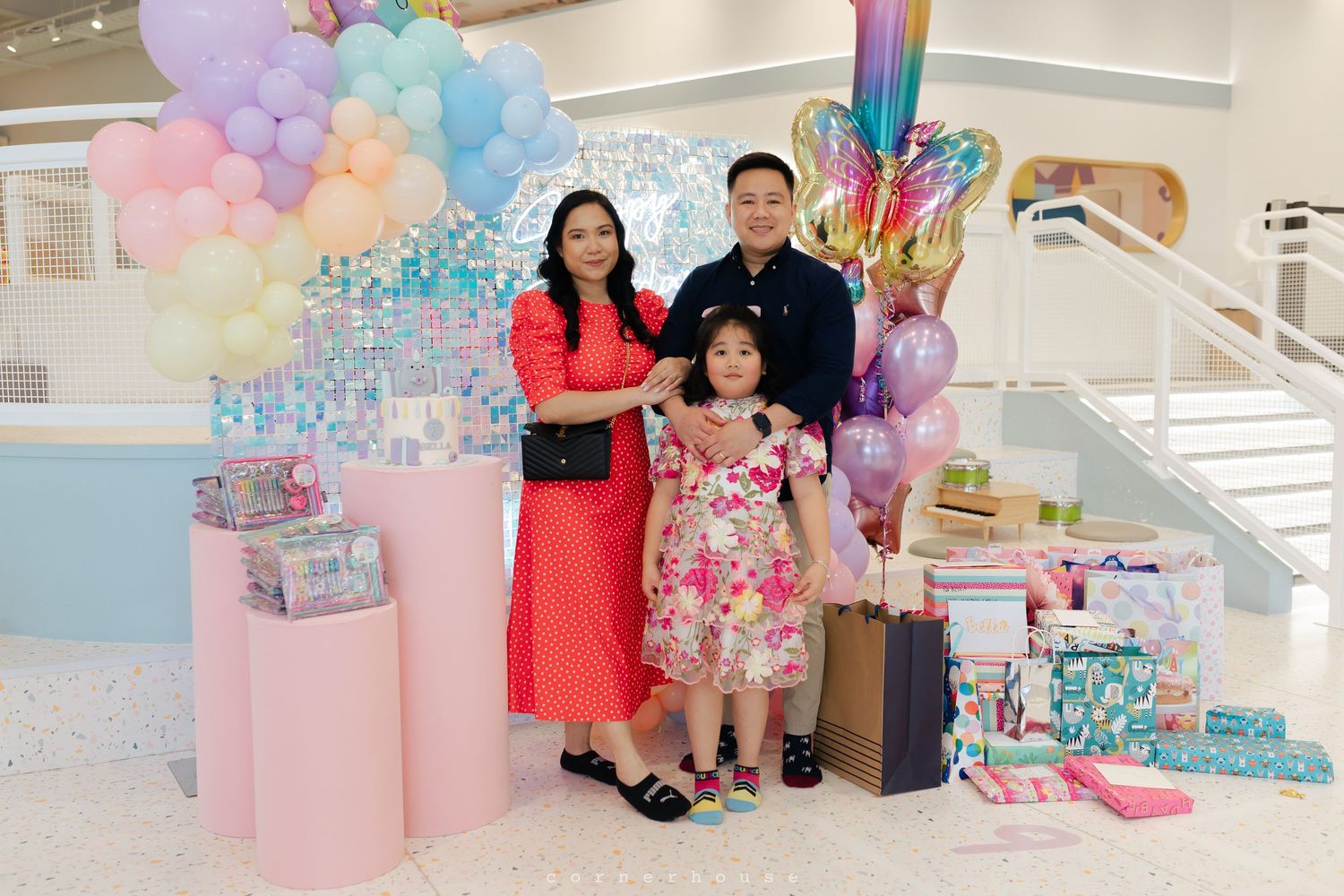 Group celebrates at a festive event with pink and blue balloons decorating the colorful party space.