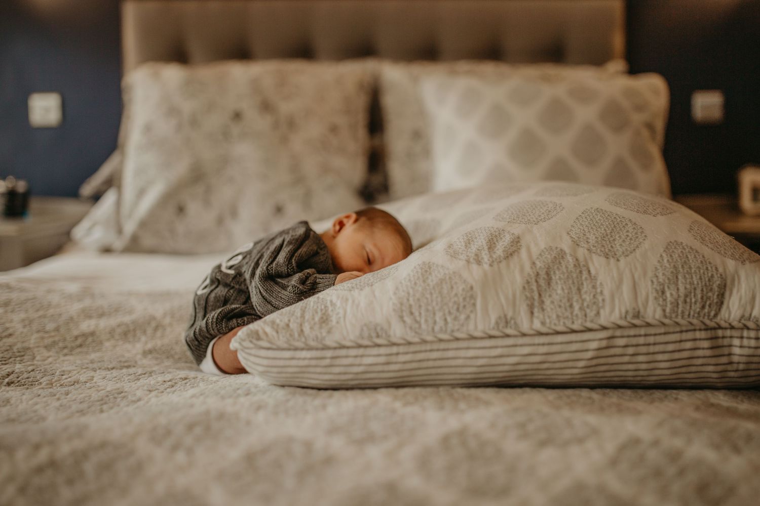 Overhead view of a newborn  sleeping peacefully in a cozy bed with rumpled gray bedding.