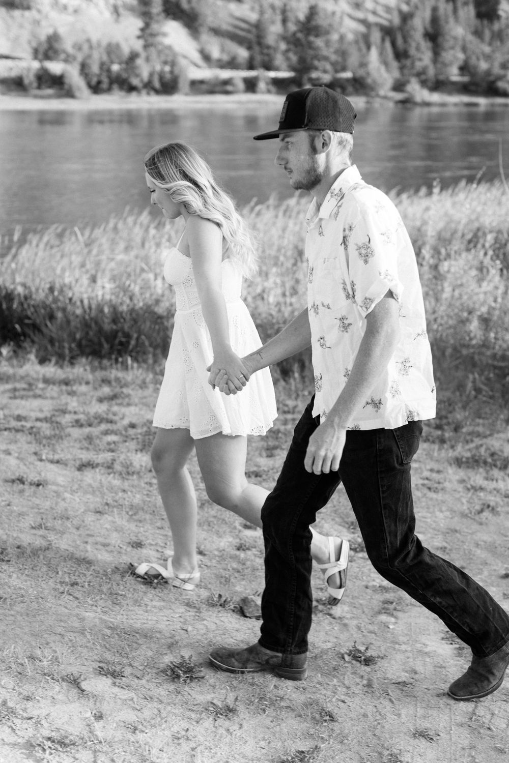 Black and white photo of couple walking playfully along a lakeside path.