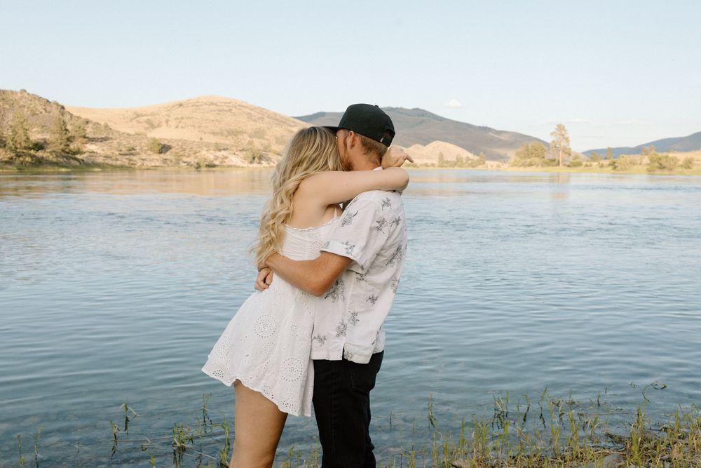 Couple embraces by serene mountain lake during golden hour.