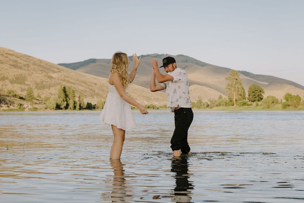 Couple poses in knee-deep lake water with scenic mountain views.