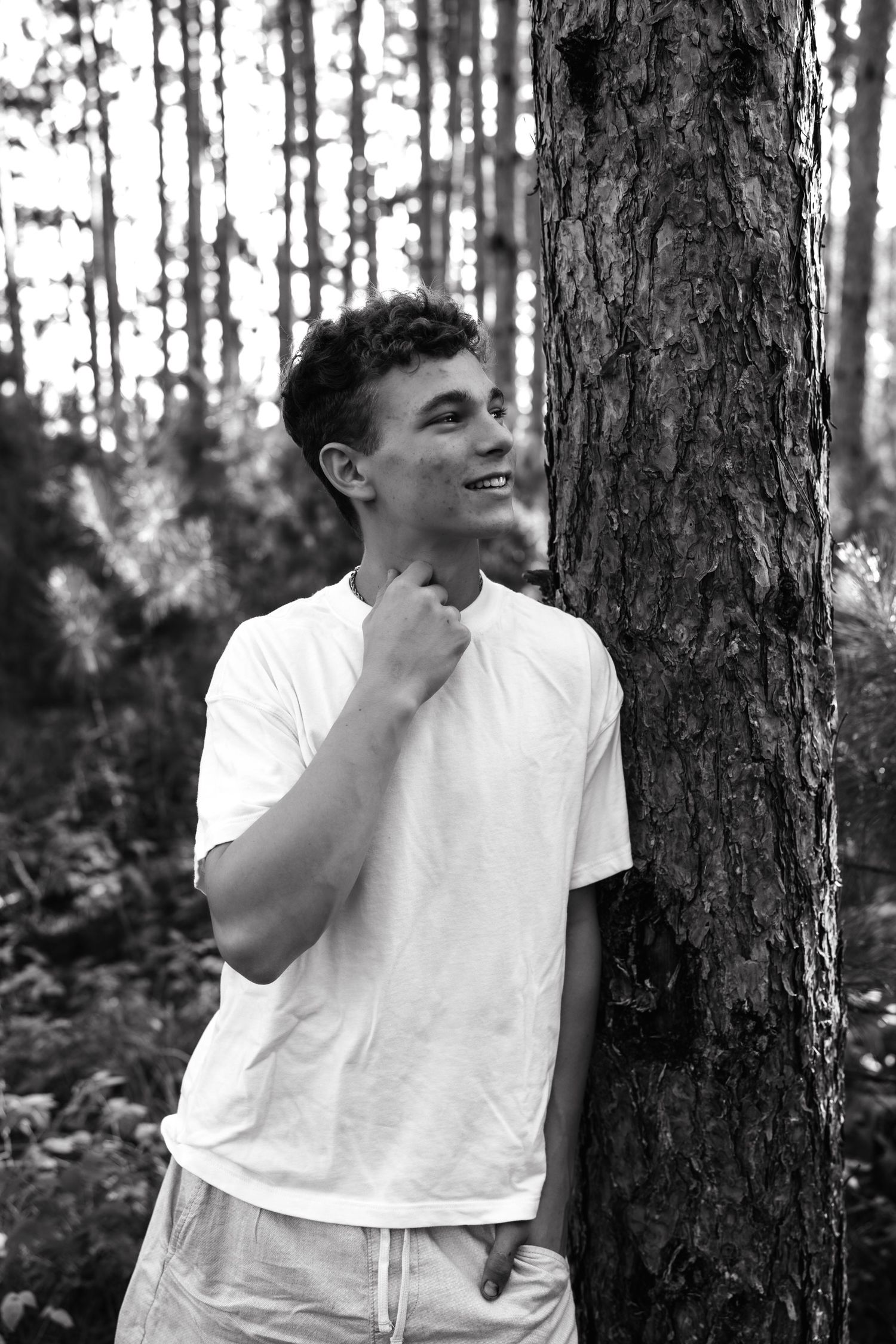 Black and white photo of person in white t-shirt laughing while standing among trees in a forest.