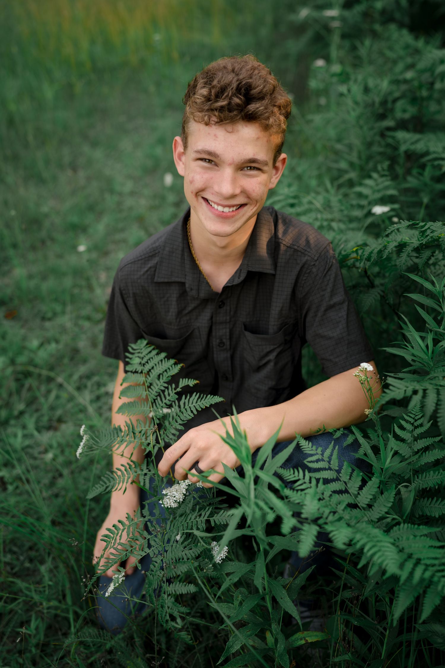 Portrait amidst lush ferns and greenery wearing a dark button-up shirt on a summer day.