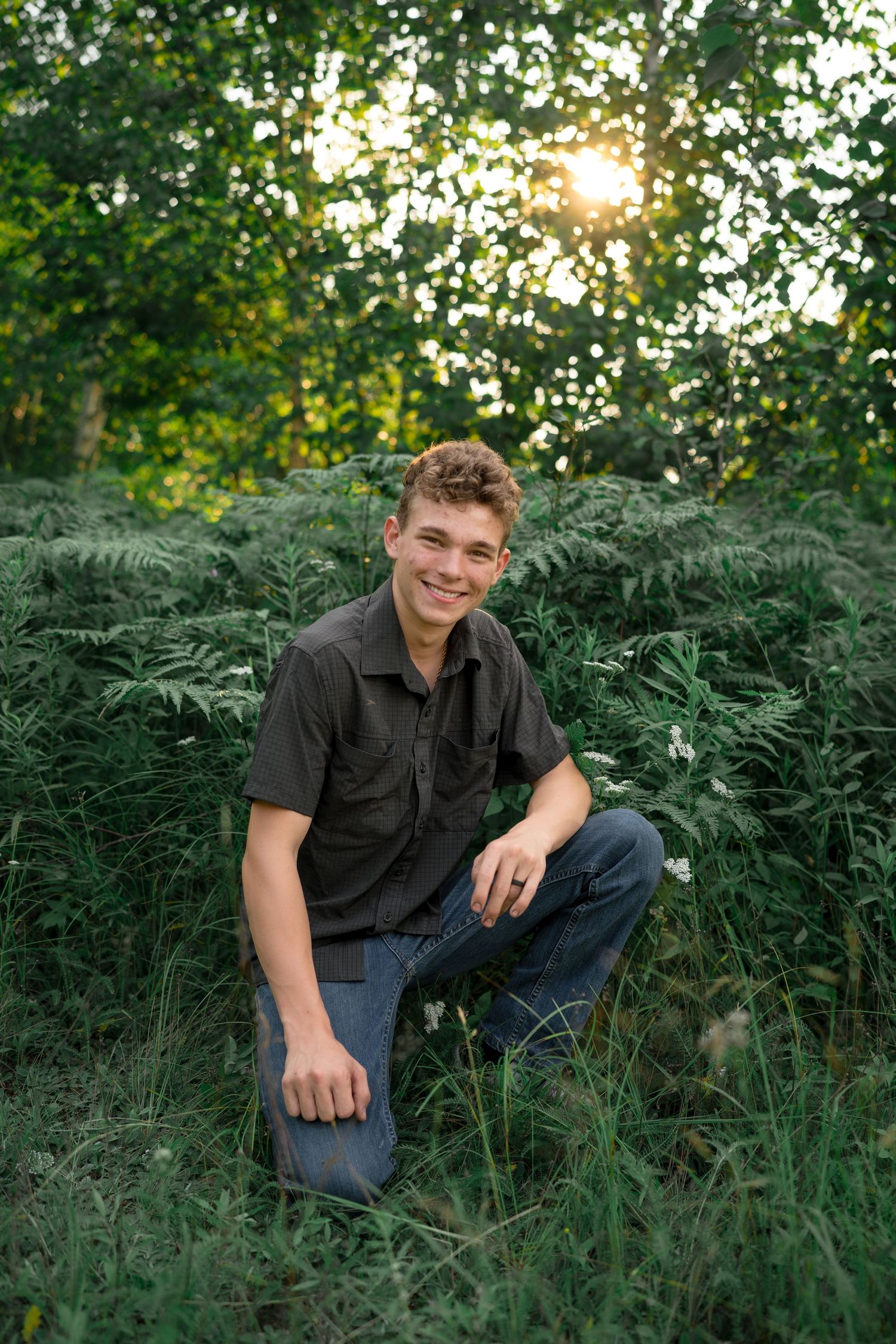 Outdoor portrait in a lush fern-filled setting with sunlight filtering through trees at golden hour.