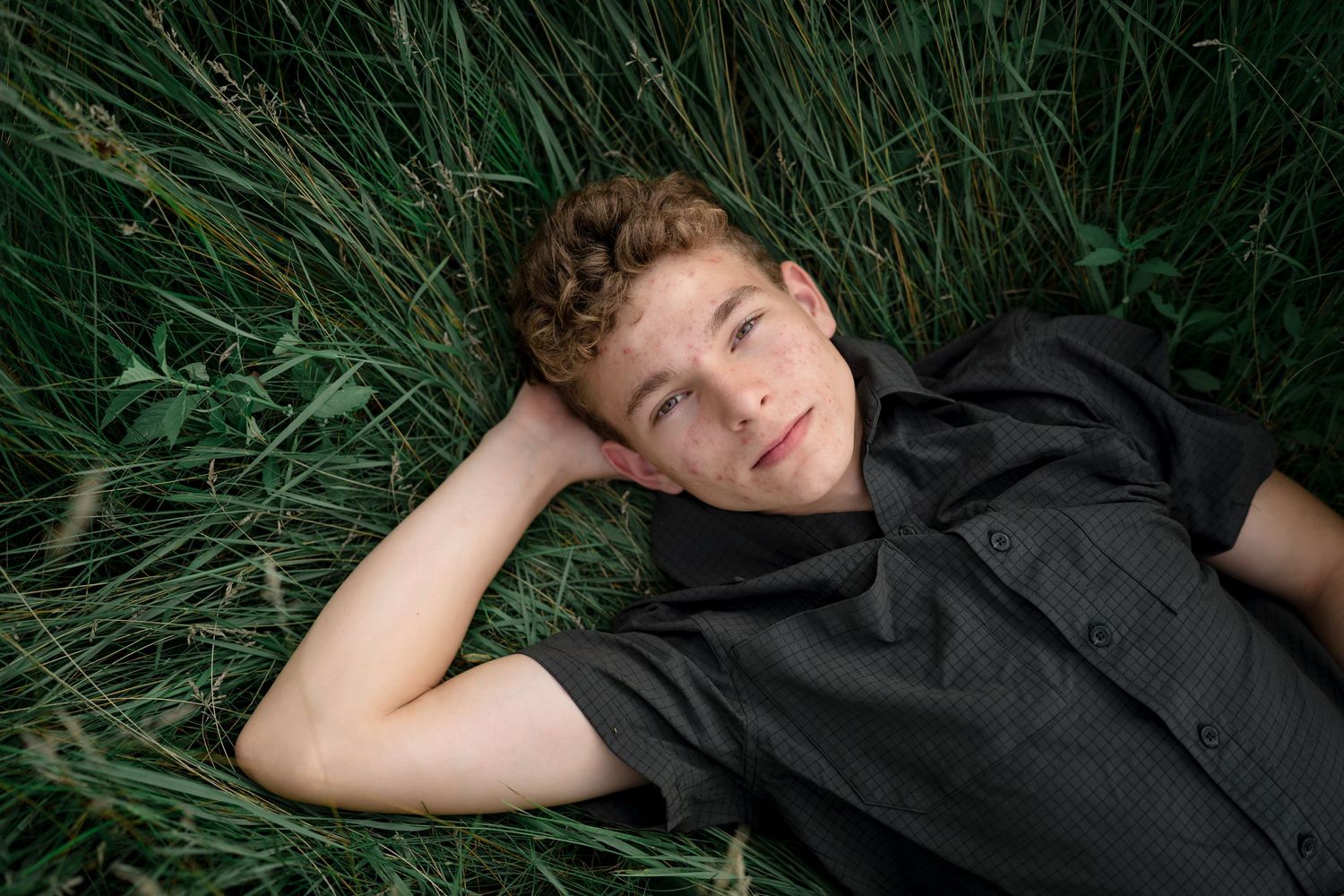 A person lies in tall grass while wearing black clothing and enjoying a peaceful moment outdoors.