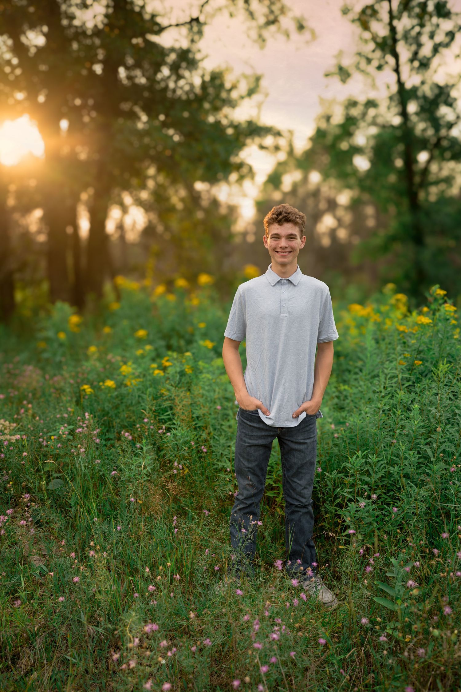 Portrait in a meadow of yellow wildflowers during sunset with trees silhouetted in the background.