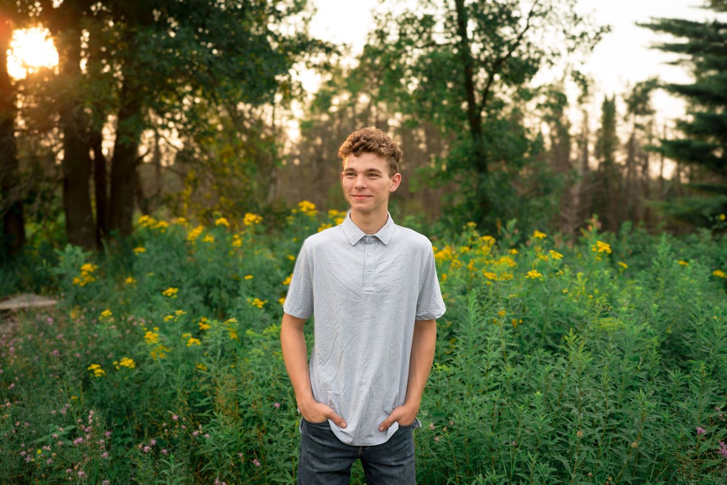 Casual outdoor portrait in a sunlit garden with yellow wildflowers and greenery at golden hour.