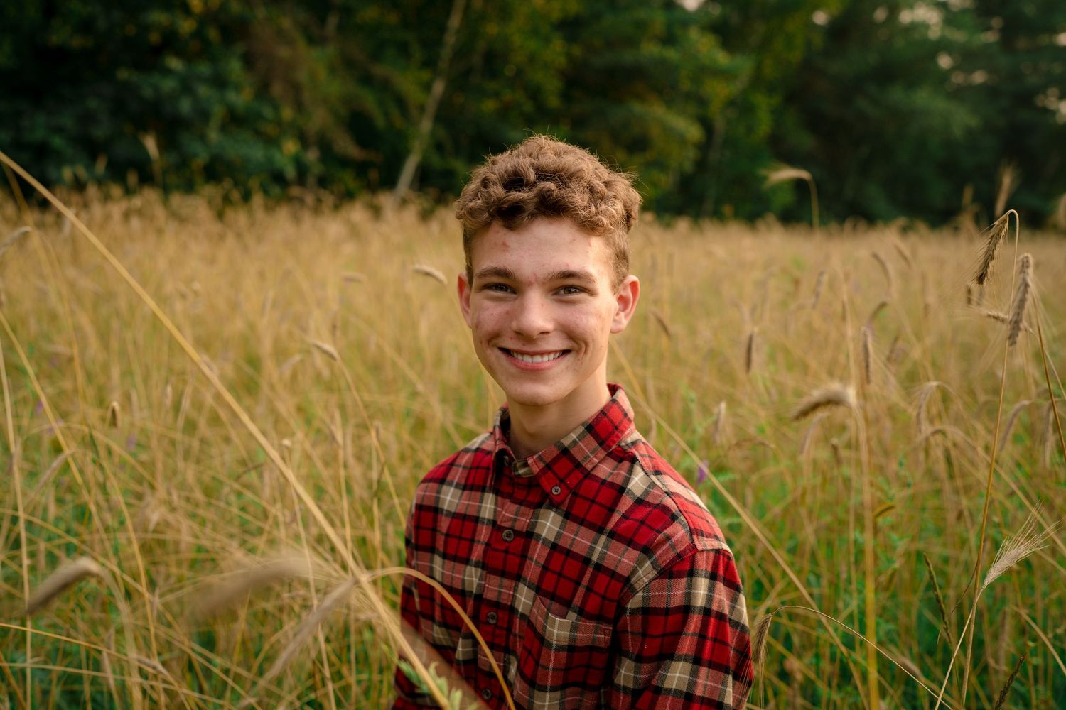 A rustic outdoor portrait of someone wearing a red plaid flannel shirt against a natural field backdrop.