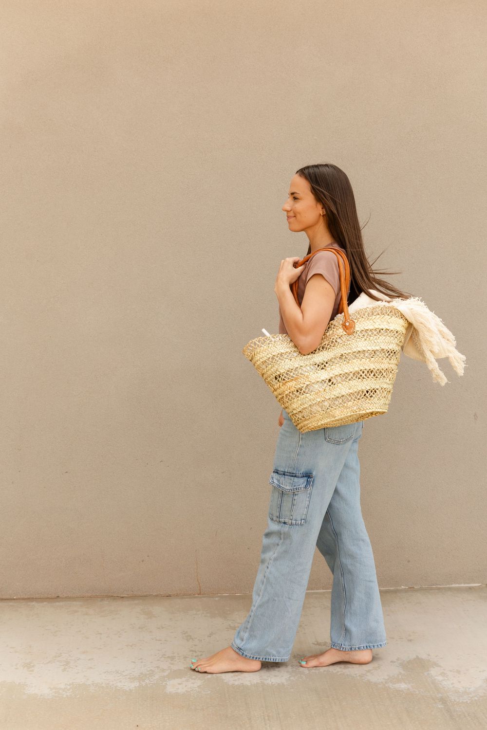 woman with wicker basket walking against a plain wall