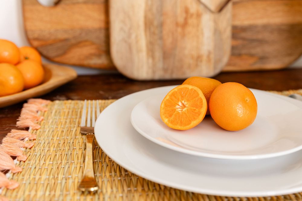 3 sliced oranges on a white plate with a fork very astheticly placed. with cutting boards and more oranges in the background