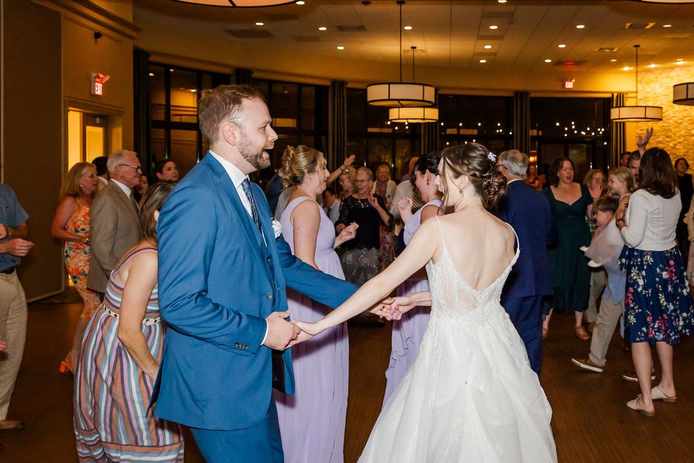 A couple in formal wedding attire dances together at their reception surrounded by wedding guests.