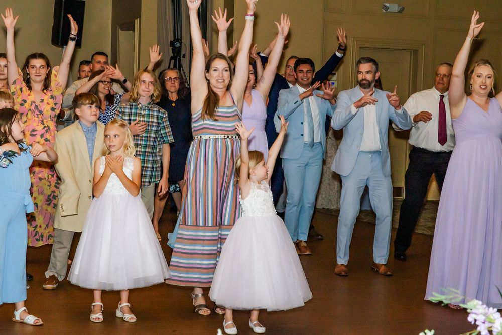 Wedding reception guests dancing with hands raised at a celebration in pastel attire on the dance floor.