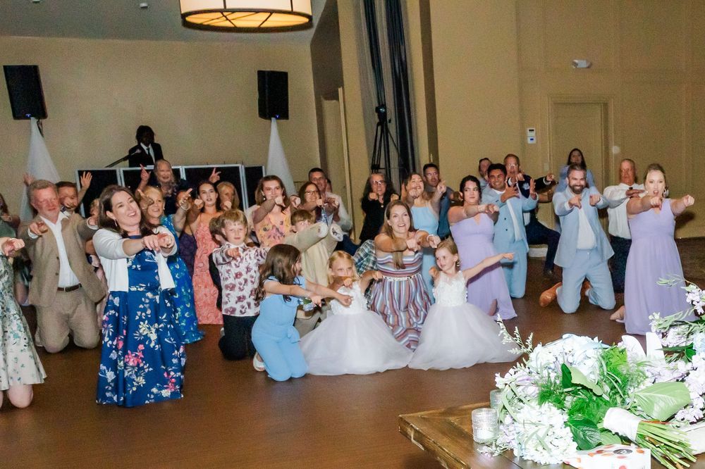 Wedding guests dancing together at a reception in formal attire while wearing floral and pastel colored dresses.