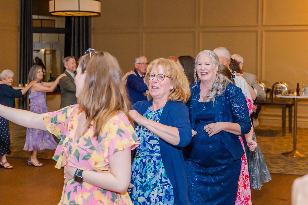 Group of people dancing and socializing at an indoor event with wood paneled walls and warm lighting.