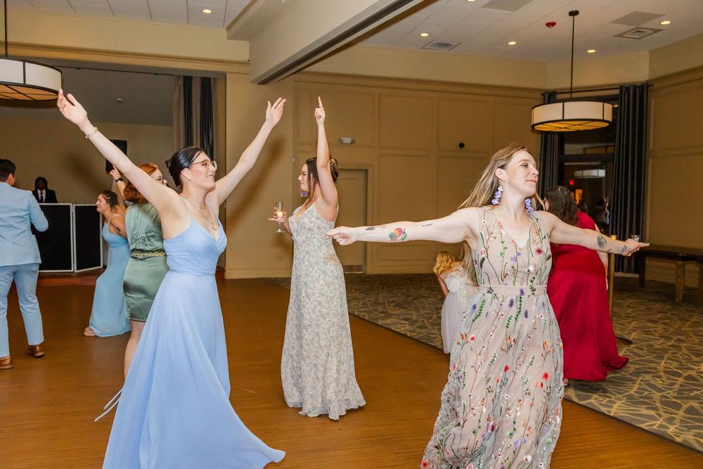 A group of dancers in flowy dresses perform choreographed movements together in a dance studio.