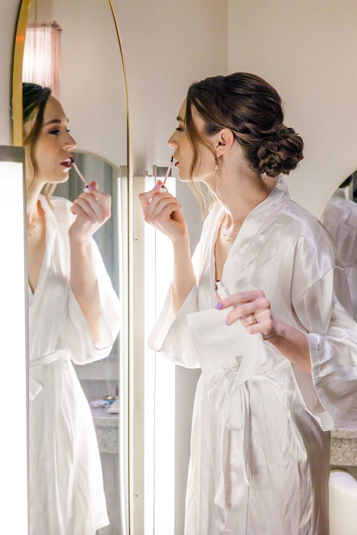 Morning wedding preparations scene with people getting ready and applying makeup in front of a bathroom mirror.