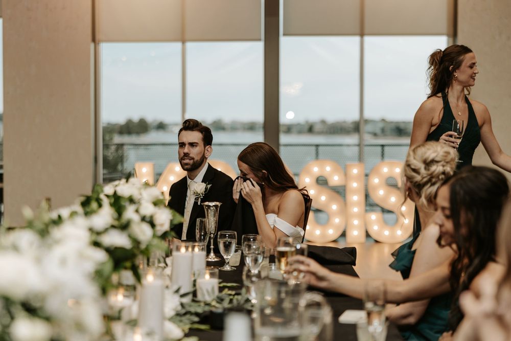 Wedding reception dinner table at sunset with elegant floral centerpieces and wine glasses in modern venue.