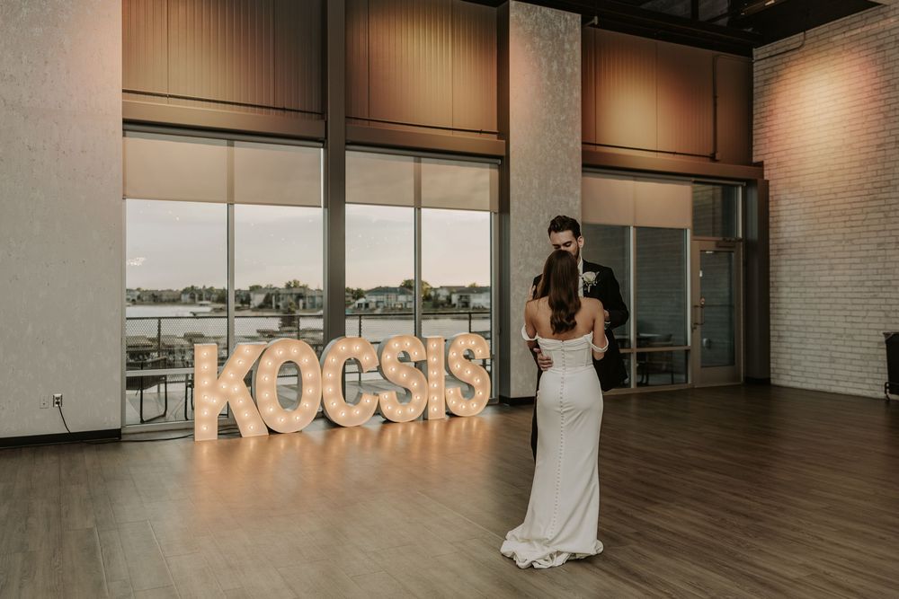 Large industrial event space with white brick walls and minimalist decor displaying illuminated KOCSIS signage.