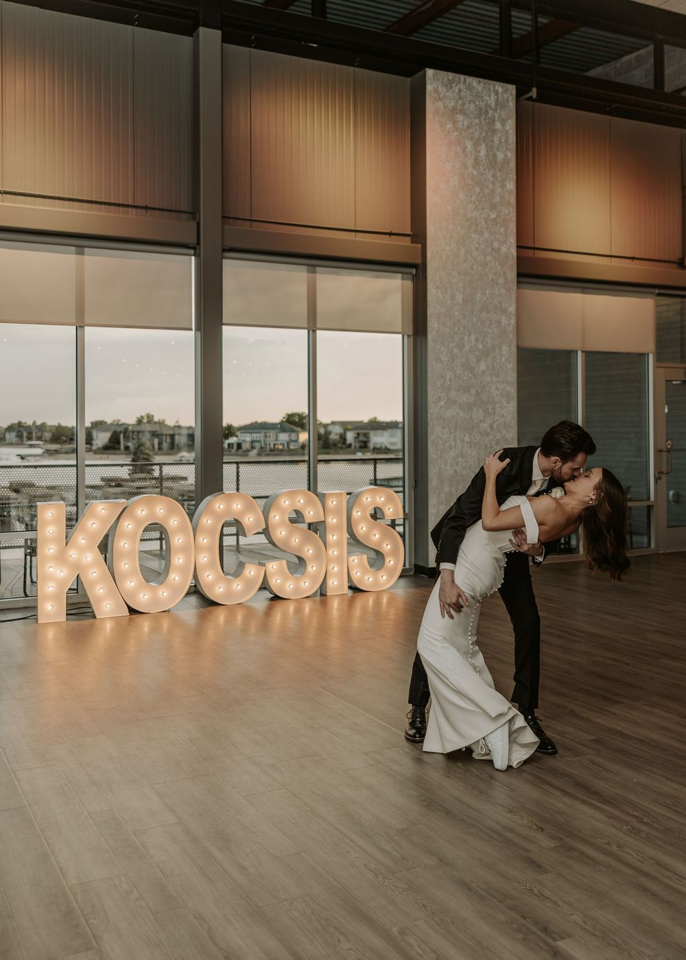 Wedding couple poses romantically in front of illuminated letter decorations during their reception.